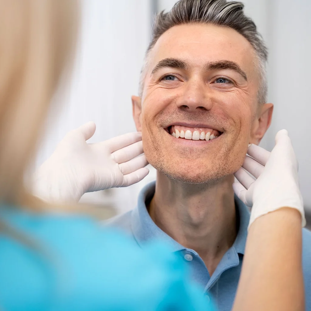 A dental professional wearing gloves examining a person’s jaw and neck area during a clinical assessment.