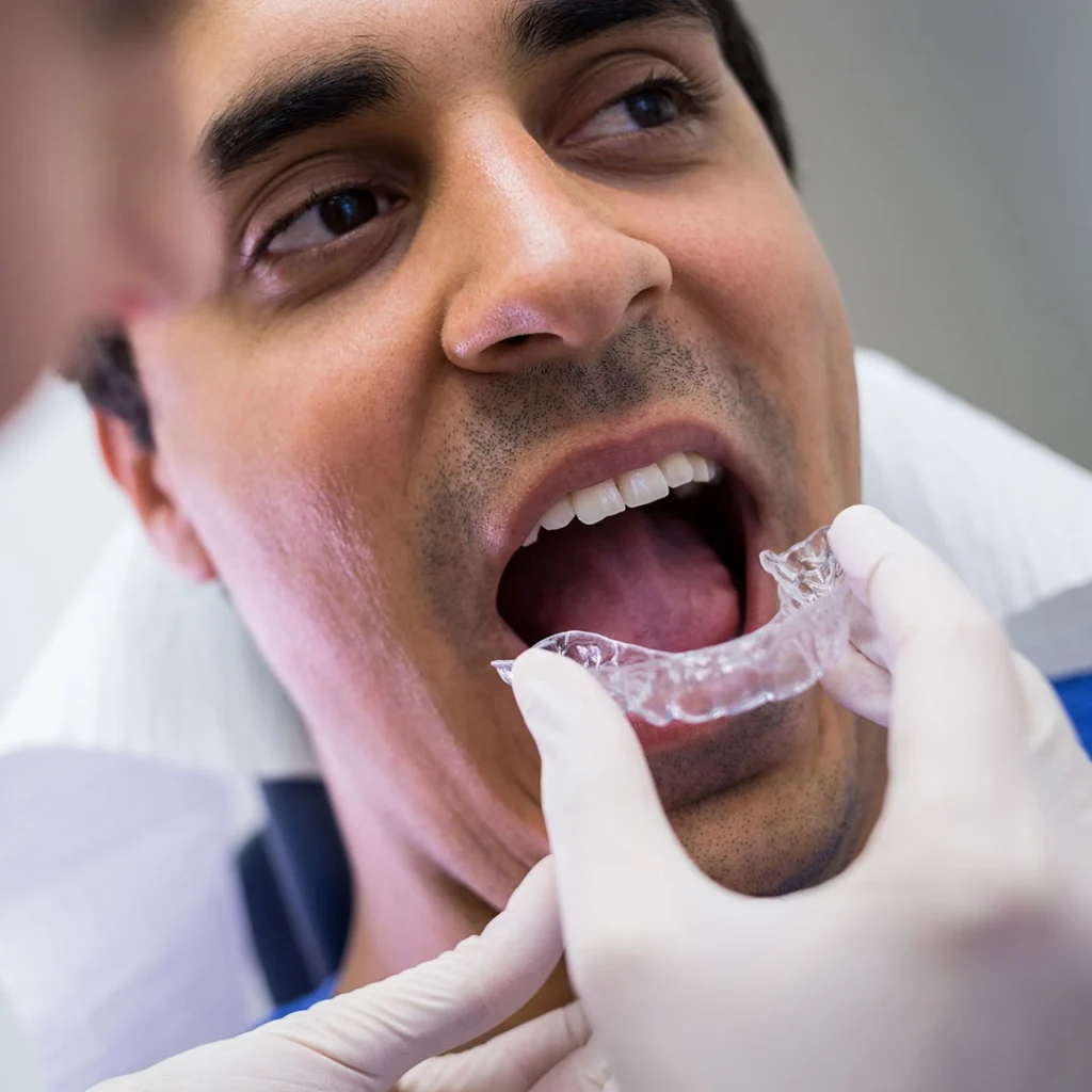 A dental professional wearing gloves adjusting a clear orthodontic aligner in a clinical setting.