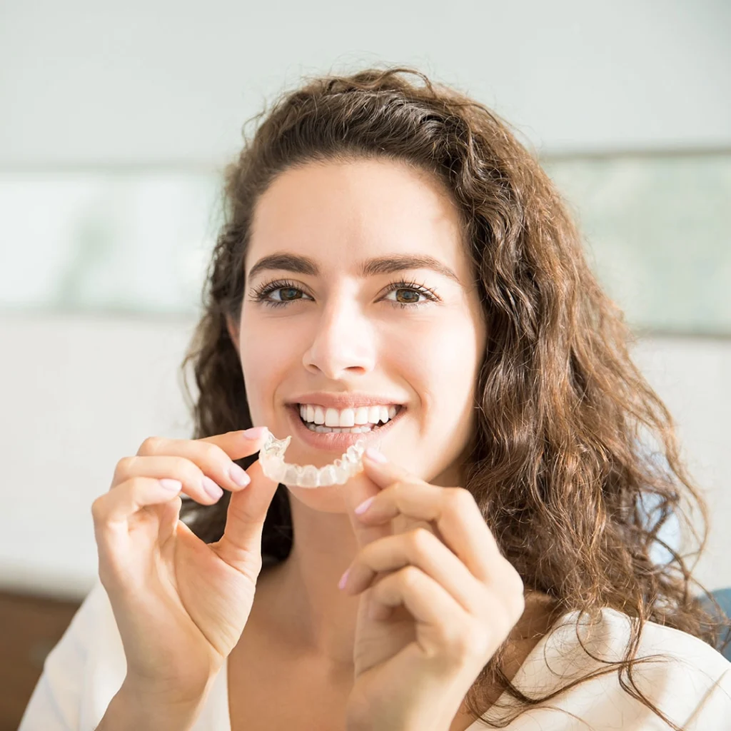 A person holding a clear orthodontic retainer in front of their mouth.