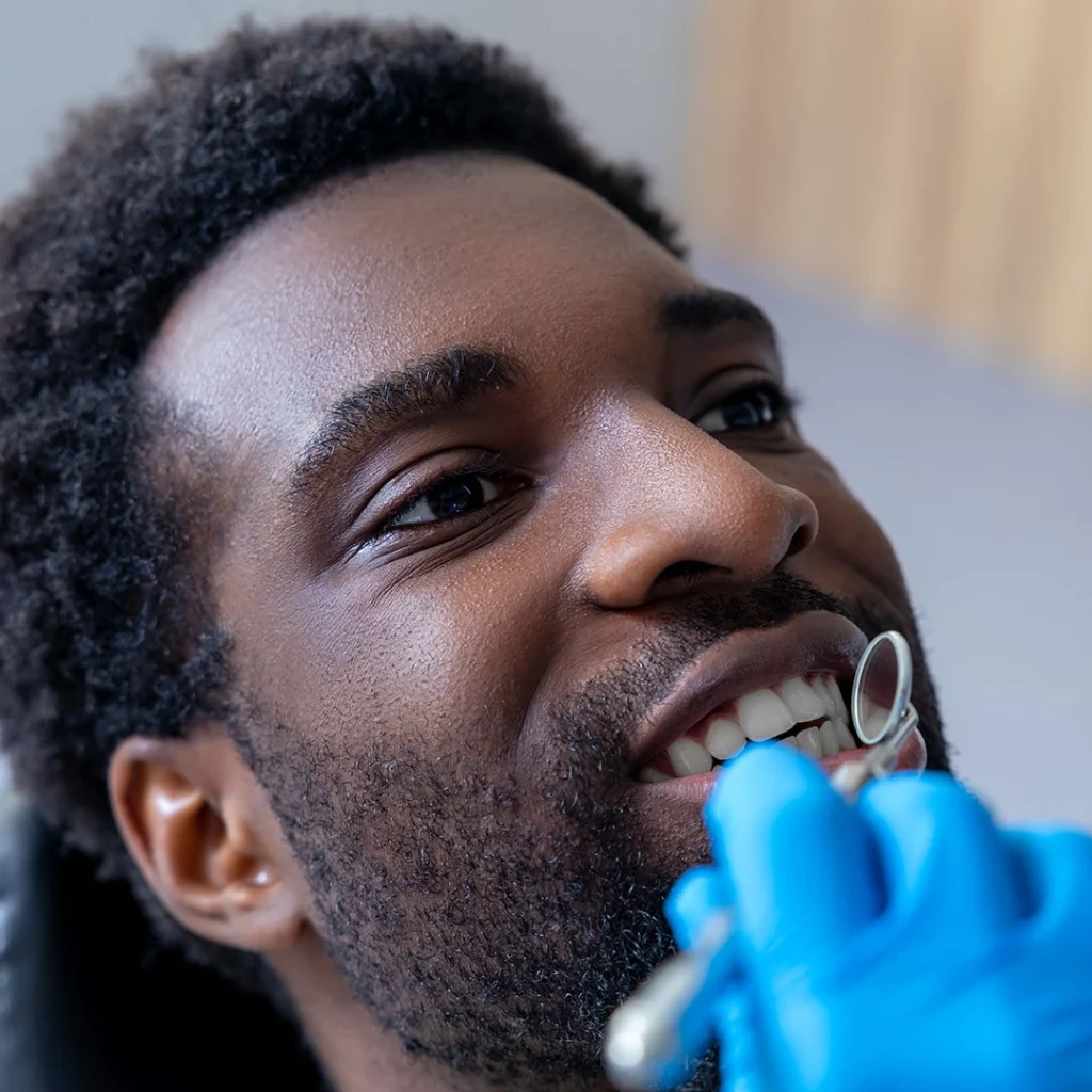 A dental professional conducting an oral examination on a patient reclined in a dental chair, with a gloved hand and dental tools visible.