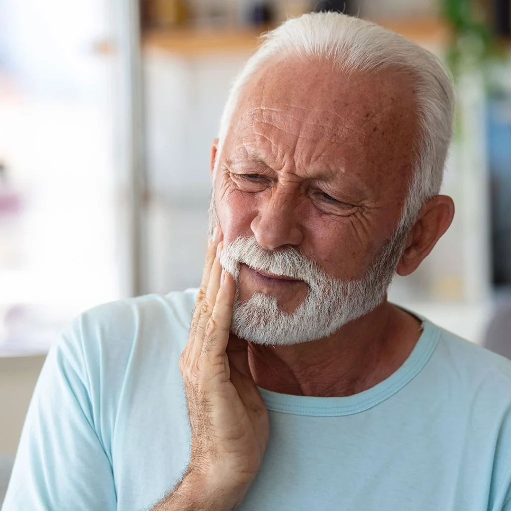 A person holding a hand to the side of their face, suggesting possible oral or jaw discomfort in an indoor environment.